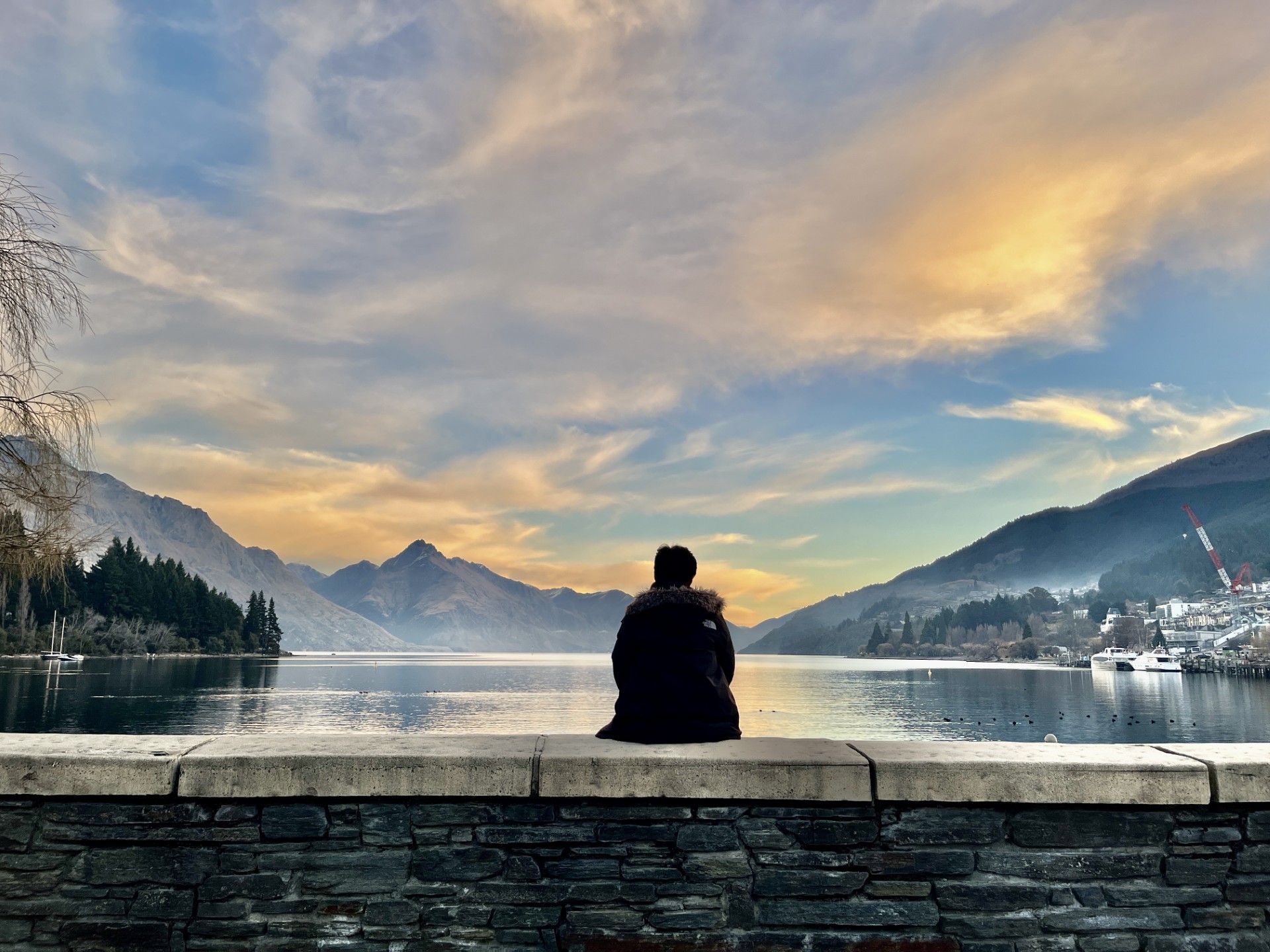 A person sitting before a lake and mountains at sunset.